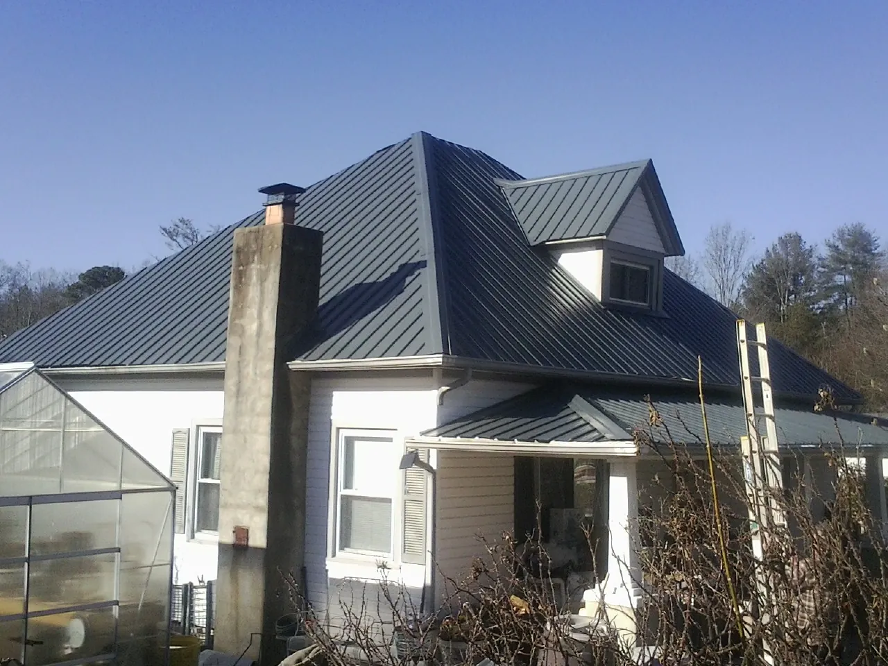 Dark blue standing seam metal roof on a white farmhouse with dormer — Slate & Tile Roof Repair by Roofing Brothers in Brentwood