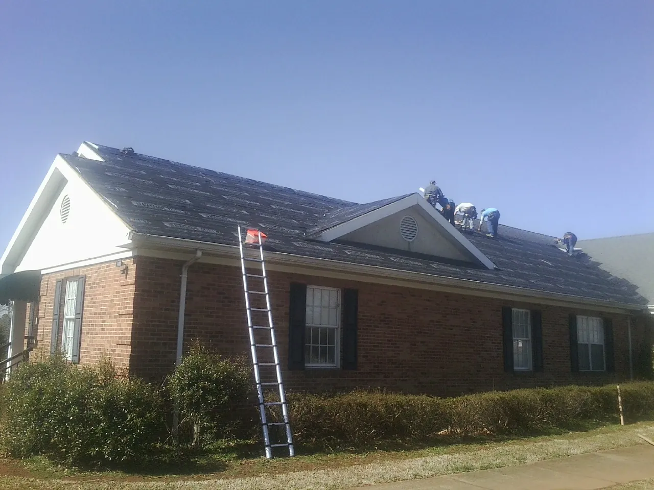 Crew tearing shingles off a brick ranch roof with a ladder set — Metal Roof Repair work by our crew in Brentwood