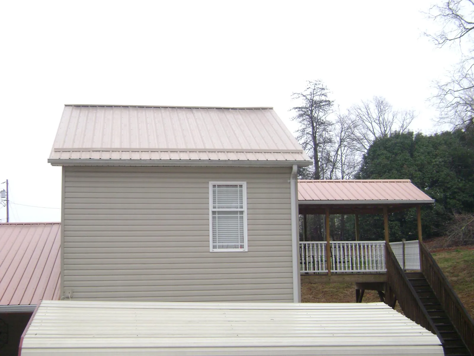 Tan metal roofs on a two story addition and attached porch, from a Roof Replacement job in Brentwood